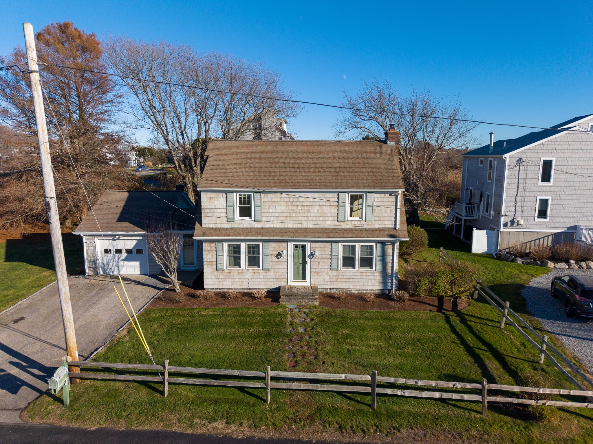 Two-story house with a brown roof and gray siding, surrounded by trees and a clear blue sky.
