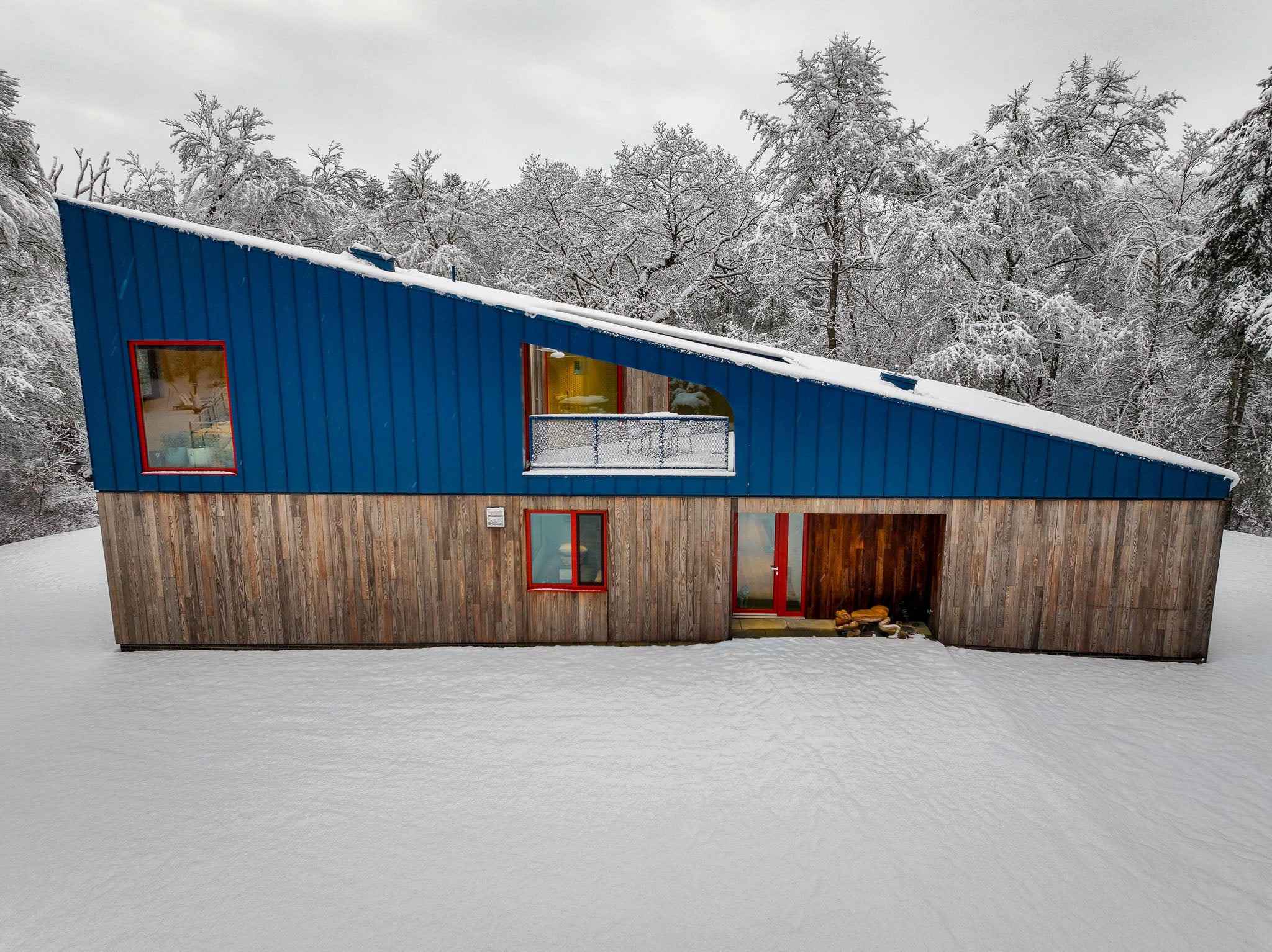 Modern house with a blue roof and wooden walls in a snowy landscape