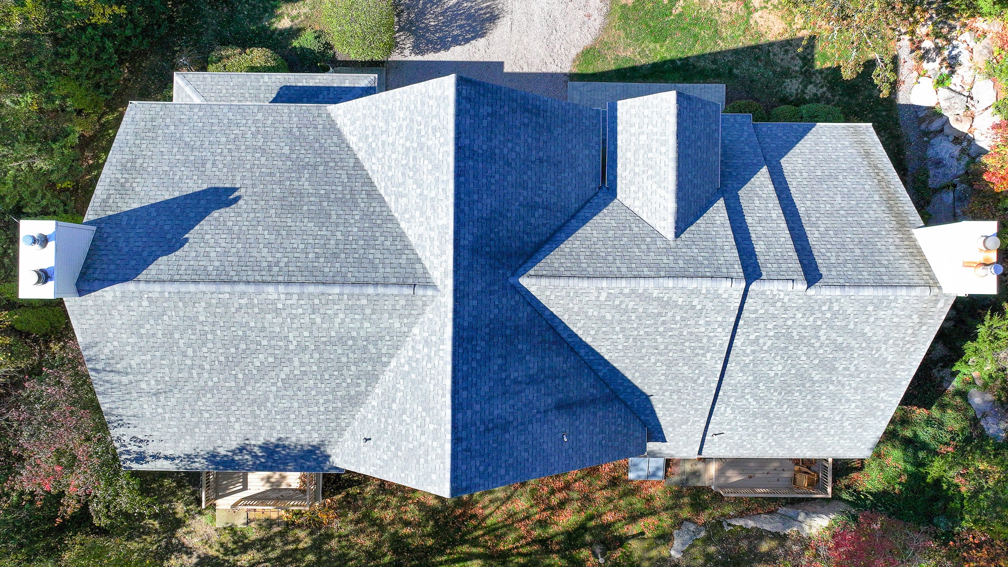 Aerial view of a house with a gray roof and white walls, surrounded by greenery.