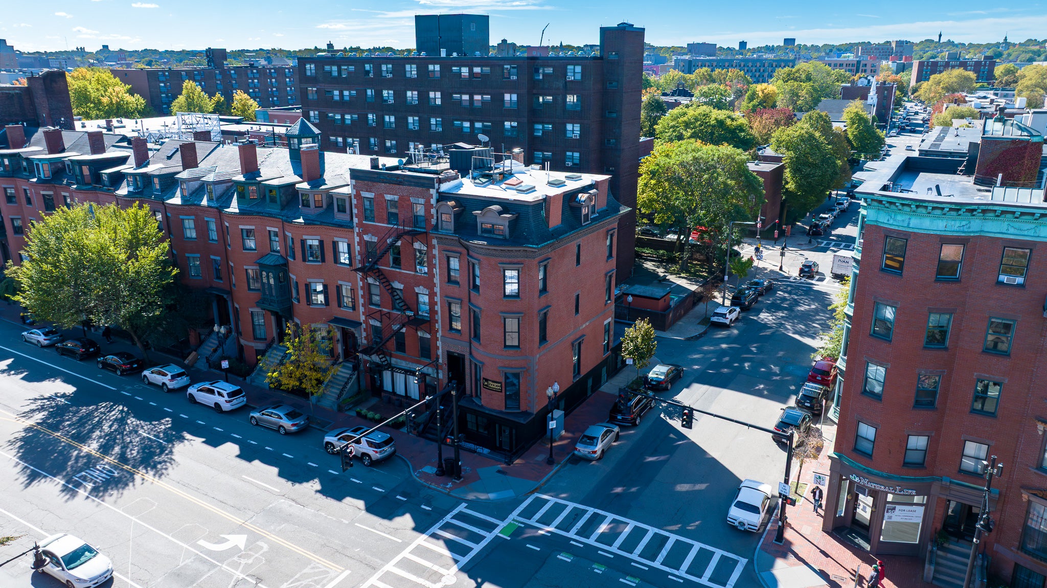Aerial view of a city street with brick buildings and parked cars.
