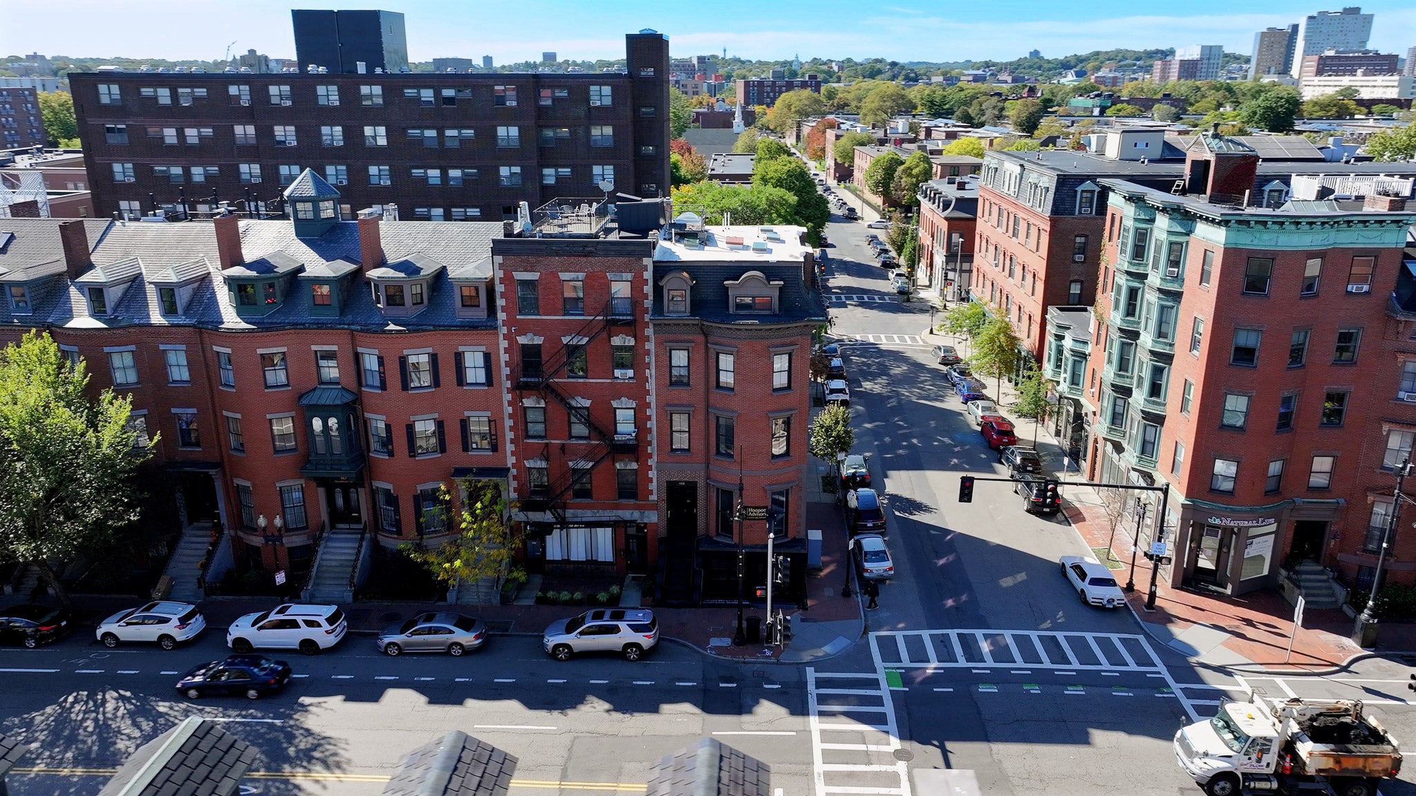 Aerial view of a city street with brick buildings and parked cars.