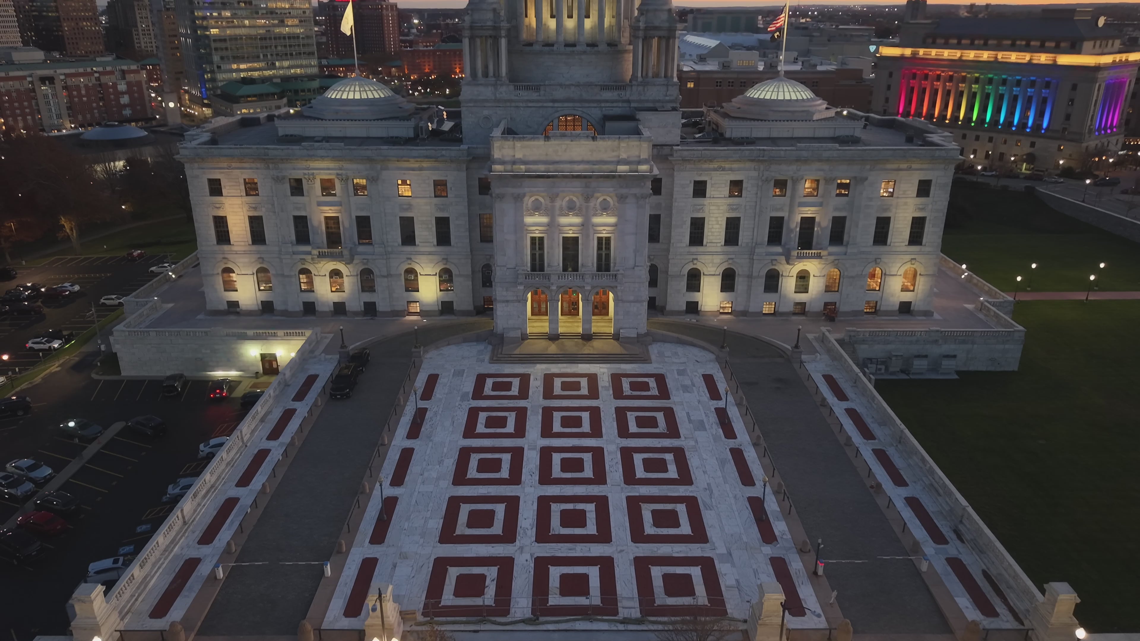 A compilation drone video showing the Rhode Island State House at sunset, an aerial orbit of a construction site, the backyard of a home with a pool, two cars with a speed ramp orbit and a pull away shot of a brick building in Boston.